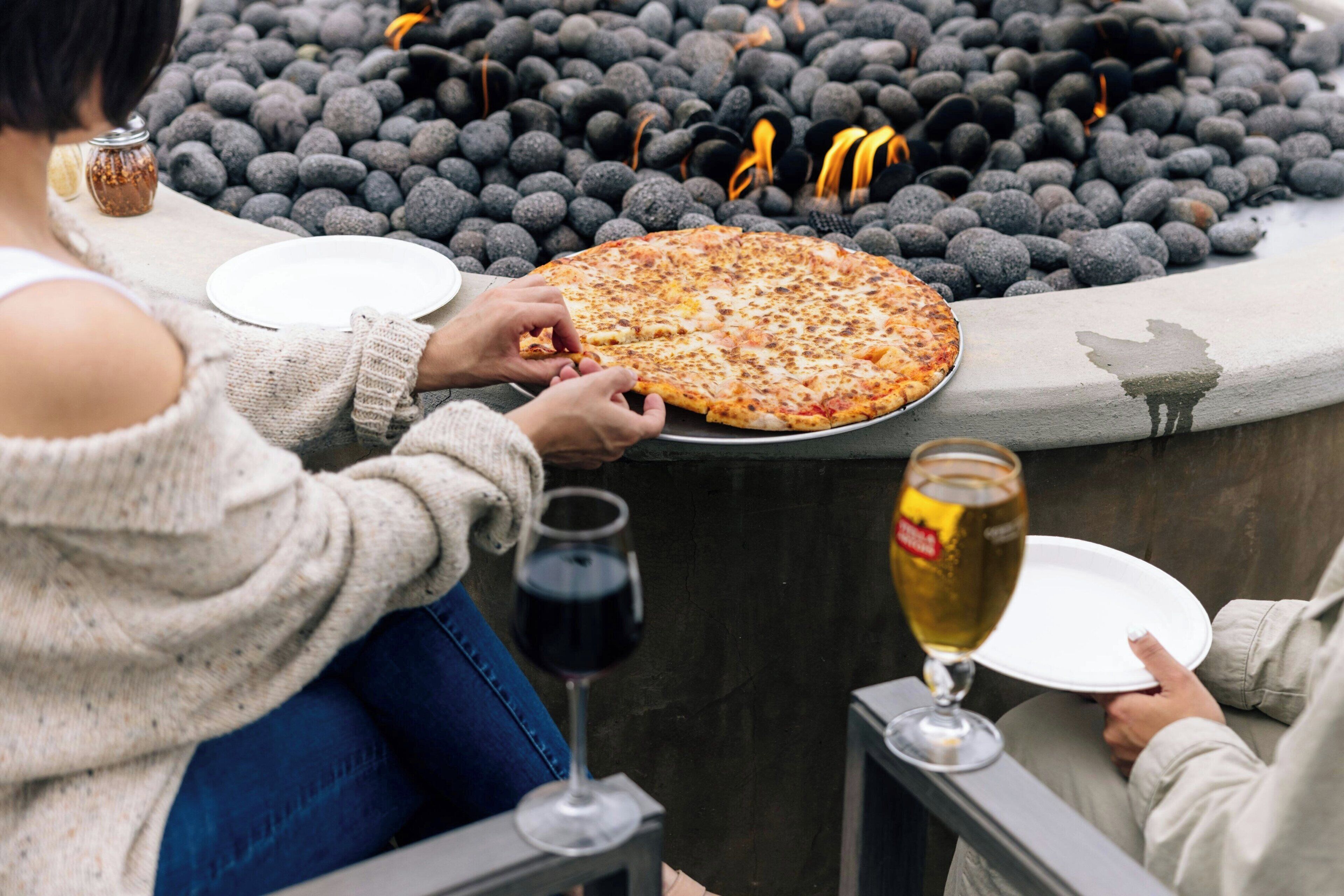 Una persona sirviendo pizza sobre una mesa de piedra rodeada por un muro de piedra.
