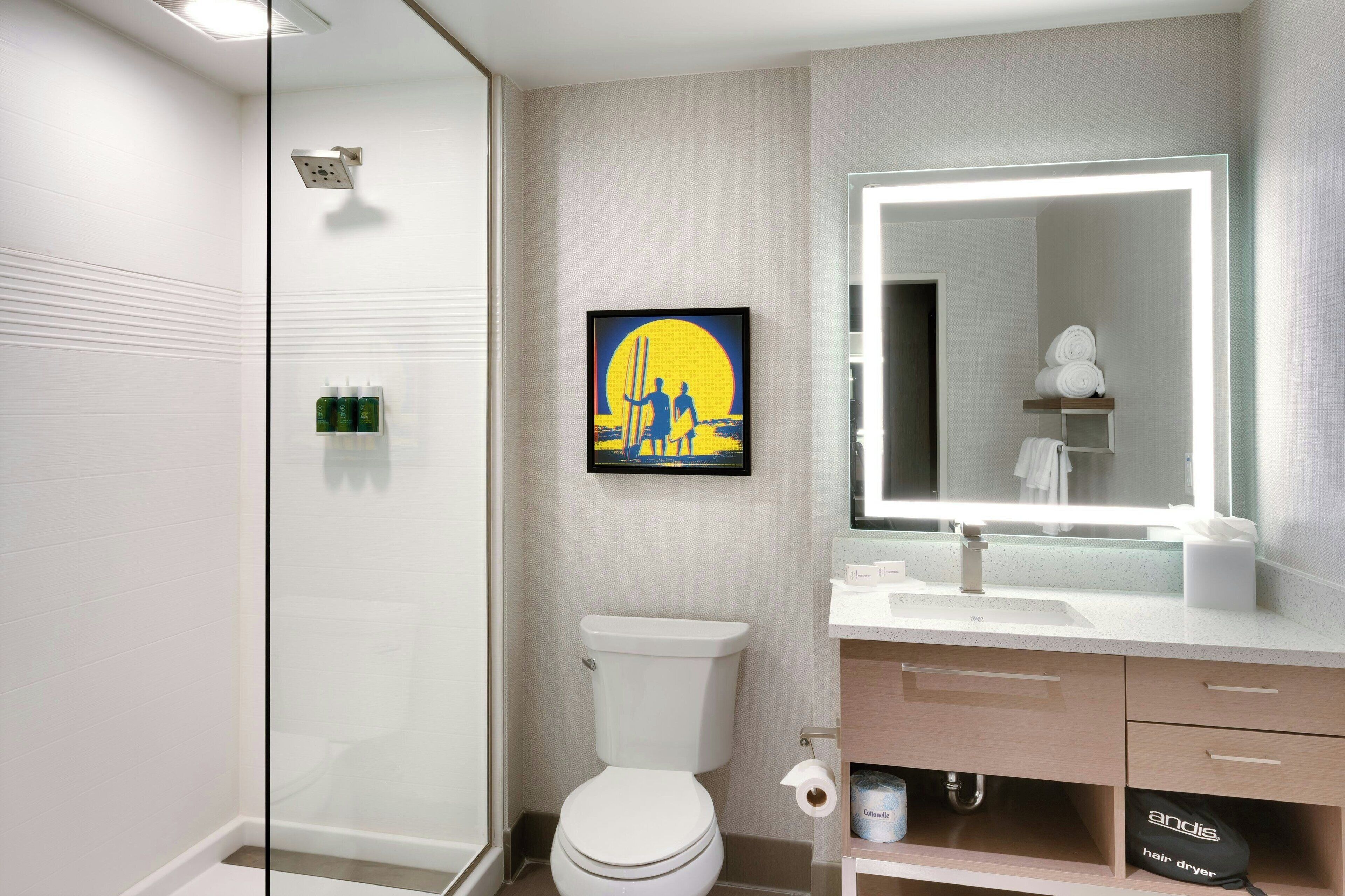 Un baño moderno con cabina de ducha de vidrio, inodoro, lavabo con espejo y una obra de arte enmarcada en la pared.