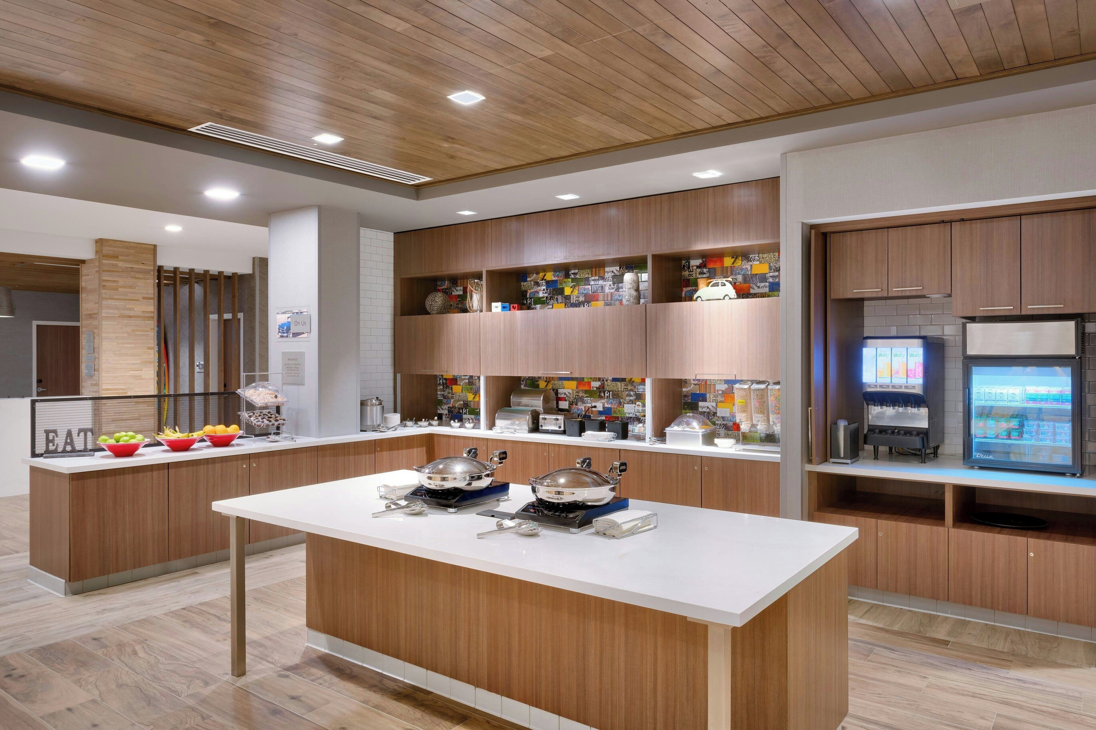 A modern kitchen with wooden cabinetry, a central island with cooking equipment, and a refrigerator with a digital display.