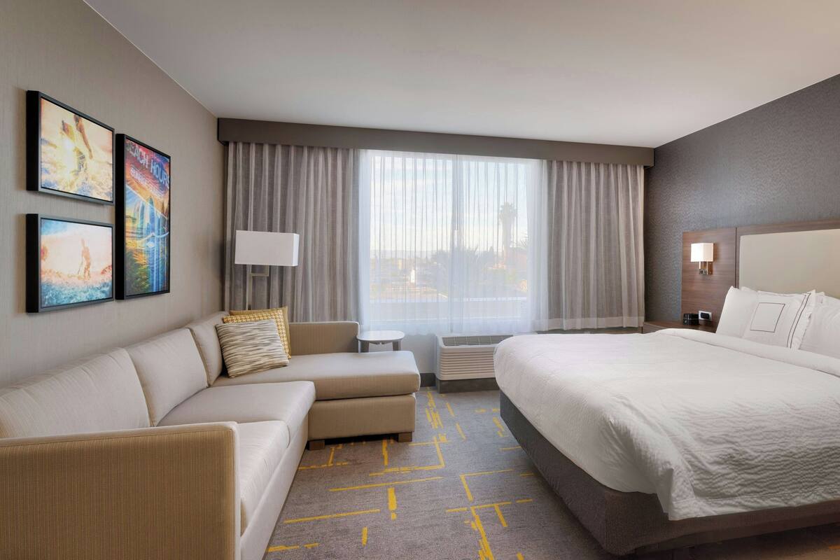 Habitación de hotel con una cama grande, un sofá, una mesita y una ventana con cortinas.