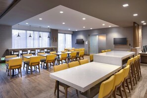 Un comedor moderno con varias mesas y sillas amarillas, un televisor de pantalla plana en la pared y suelo de madera.