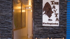 Entrada de un hotel con fachada de piedra, una puerta de madera y dos sillas de madera afuera.