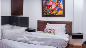 Un cuarto de hotel con una cama grande, un cuadro en la pared, una bañera y una mesita.