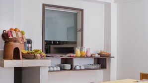 Un comedor con una mesa de madera, sillas, un televisor sobre la encimera y diversos alimentos y utensilios de cocina en la encimera.