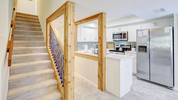 Eine moderne Küche mit weißen Schränken, Edelstahlgeräten und einer Holztreppe mit verzierten Geländern.