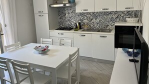 Une cuisine moderne avec des meubles blancs, une cuisinière à gaz et un four à micro-ondes. On y trouve une table à manger avec des chaises et un saladier posé dessus.