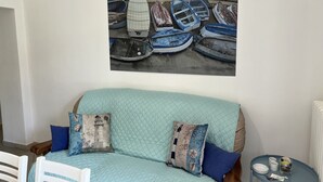 Une pièce comprenant un lit, une petite table et un tableau représentant des bateaux, accroché au mur.