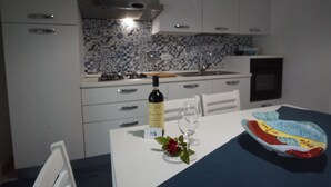 Une cuisine moderne avec des meubles blancs, un pare-feu décoratif et une table à manger agrémentée d’une bouteille de vin, d’un verre et d’objets décoratifs.