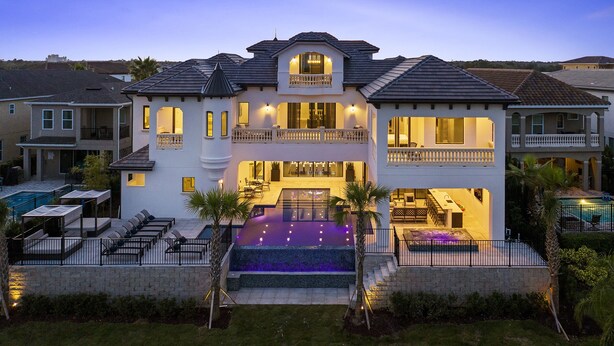 A large, two-story house with a swimming pool, multiple balconies, and a well-lit exterior.