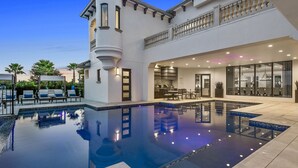 A luxurious pool area with a clear view of the pool, lounge chairs, and a modern kitchen visible through the glass doors.