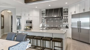 A modern kitchen with white cabinetry, stainless steel appliances, and a central island with bar stools.