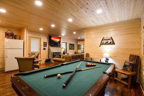A pool table in a wooden room with a fireplace, a television, and a framed picture on the wall.