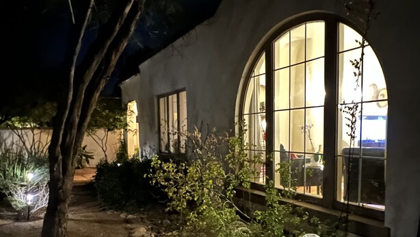 A nighttime view of a building with large arched windows, a stone pathway, and various plants. - Timeless Elegance ~ 1920's Sam Hughes Casita Mariposa ~ Walk to UA! Parking (Tucson)