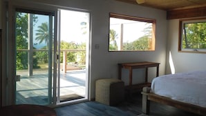 Un dormitorio con cama, ventilador de techo, mesa, banco y vistas a través del ventanal corredero.