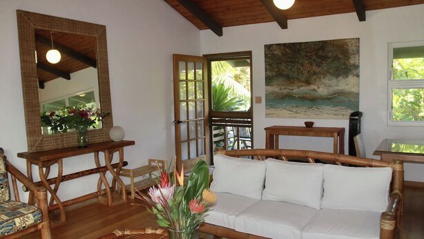 Una habitación con techo de madera, un sofá blanco, una mesa de madera, un espejo y un cuadro.