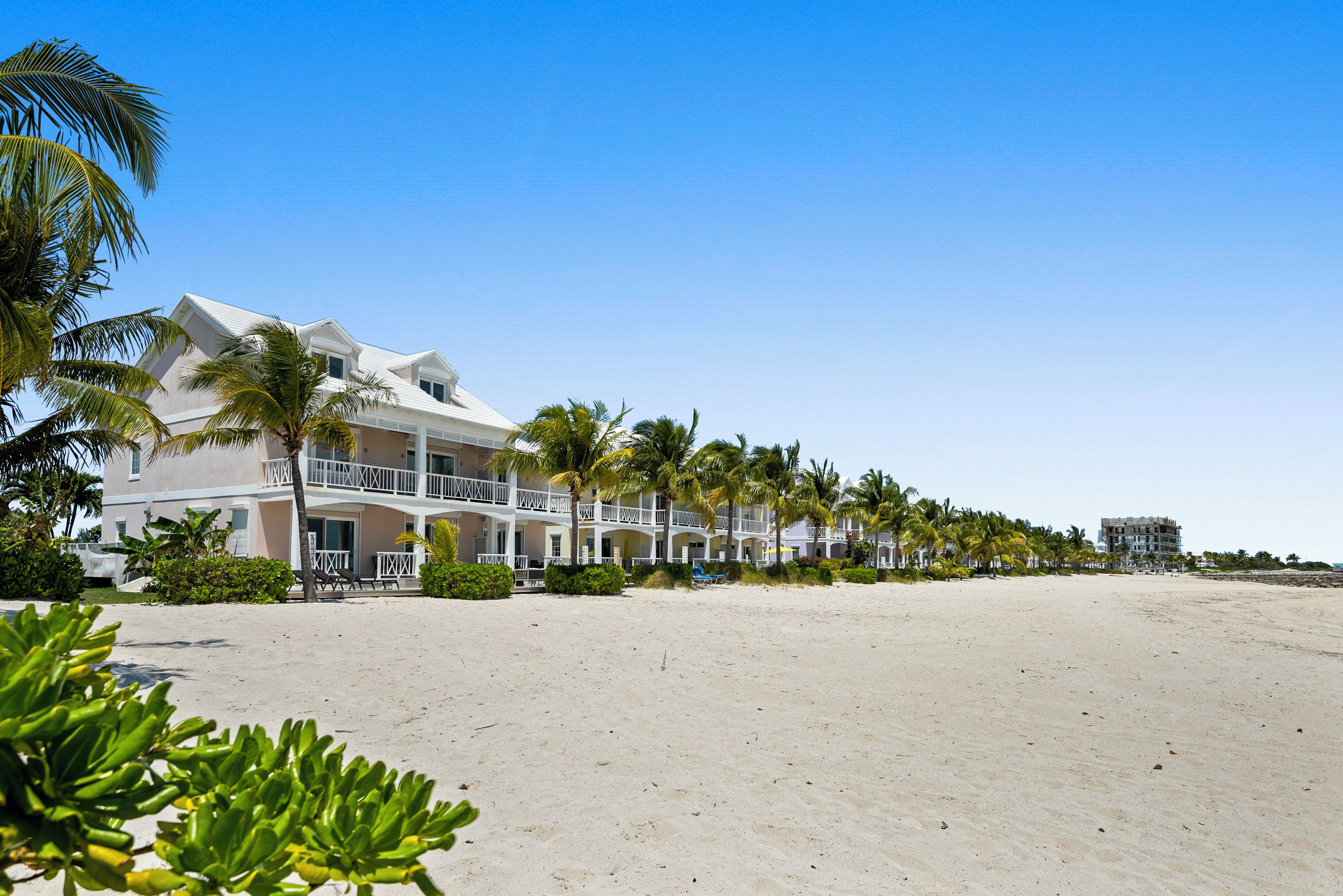 A beachfront hotel with multiple balconies, palm trees, and a sandy beach.