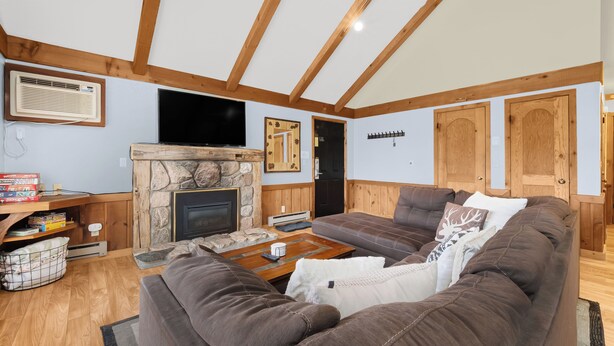 Una sala de estar acogedora con chimenea de piedra, vigas de madera, un sofá marrón grande y un televisor de pantalla plana.
