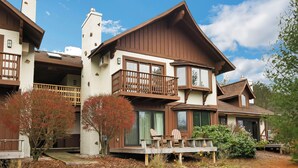 A two-story house with a balcony, large windows, and a deck with chairs.