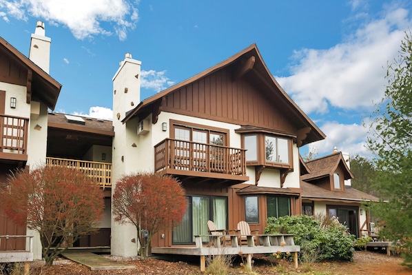 A two-story house with a balcony, large windows, and a deck with chairs.