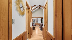 A wooden hallway with a high ceiling and skylights, leading to a kitchen area with wooden cabinets and a dining table.