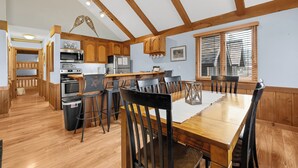 A modern kitchen with wooden beams, a dining area with a wooden table and chairs, and a view of the city through large windows.