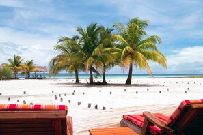 Une plage bordée de palmiers et dotée d’une terrasse en bois avec des coussins à rayures rouges.
