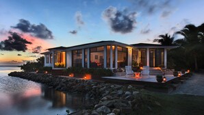 Ein modernes Haus mit Glasfassade, einer Terrasse mit Sitzgelegenheiten und Blick auf den Ozean.
