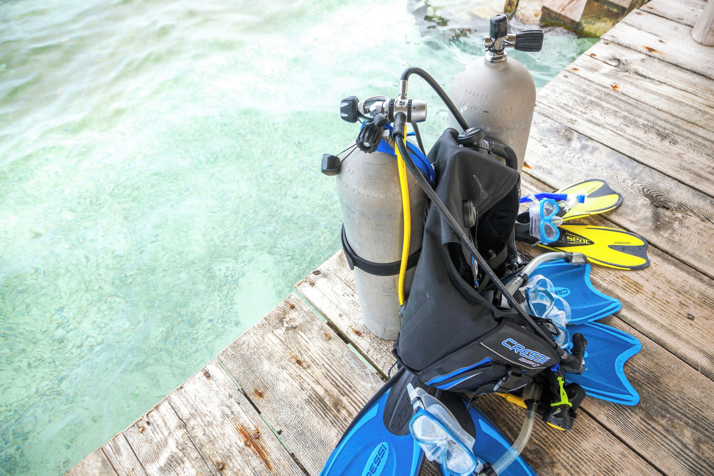 A wooden dock with a scuba diving setup including a tank, fins, and a mask.