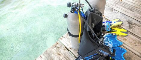 A wooden dock with a scuba diving setup including a tank, fins, and a mask.