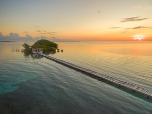 Ein friedlicher Sonnenuntergang über einem ruhigen Meer mit einem hölzernen Steg, der zu einer kleinen Insel mit einer Laube führt.