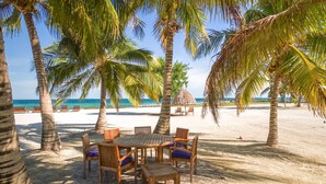 Eine Strandkulisse mit einem Holztisch und Stühlen, Palmen und Blick aufs Meer.