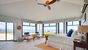 Amplia habitación con una cama grande, ventilador de techo y vista a la playa.