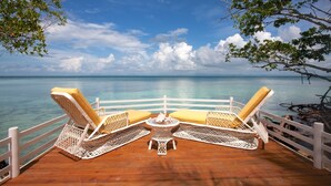 Terraza con dos sillones de mimbre y una mesita pequeña, con vista al mar azul y despejado.