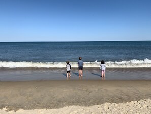 Tre børn står på en sandstrand og ser ud over havet.