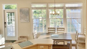 Un espace repas avec une table et des chaises en bois, de grandes fenêtres équipées de stores et un luminaire suspendu.