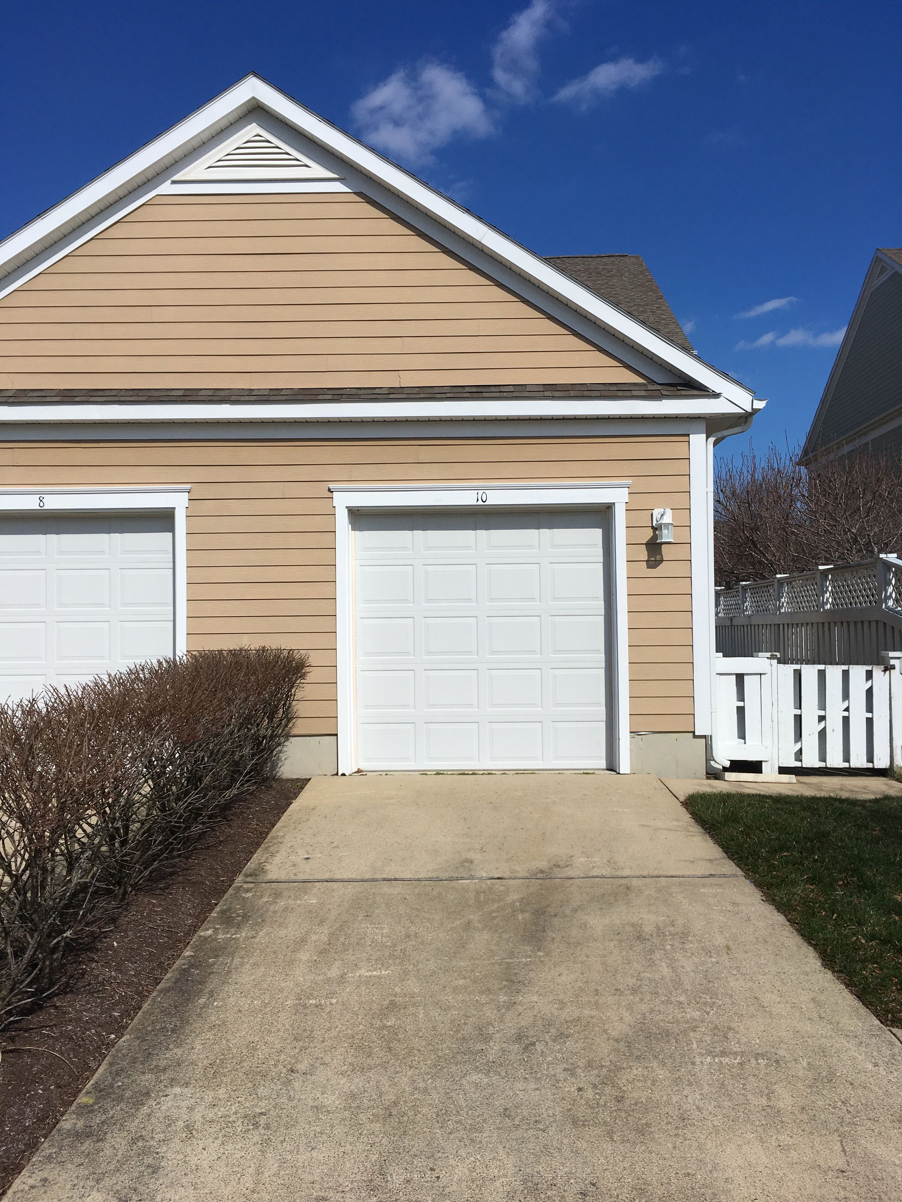A two-story house with a beige exterior, two garage doors, and a white picket fence.