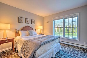 Une chambre avec un grand lit, deux tables de chevet avec des lampes, une fenêtre donnant sur l’extérieur et trois tableaux encadrés accrochés au mur.