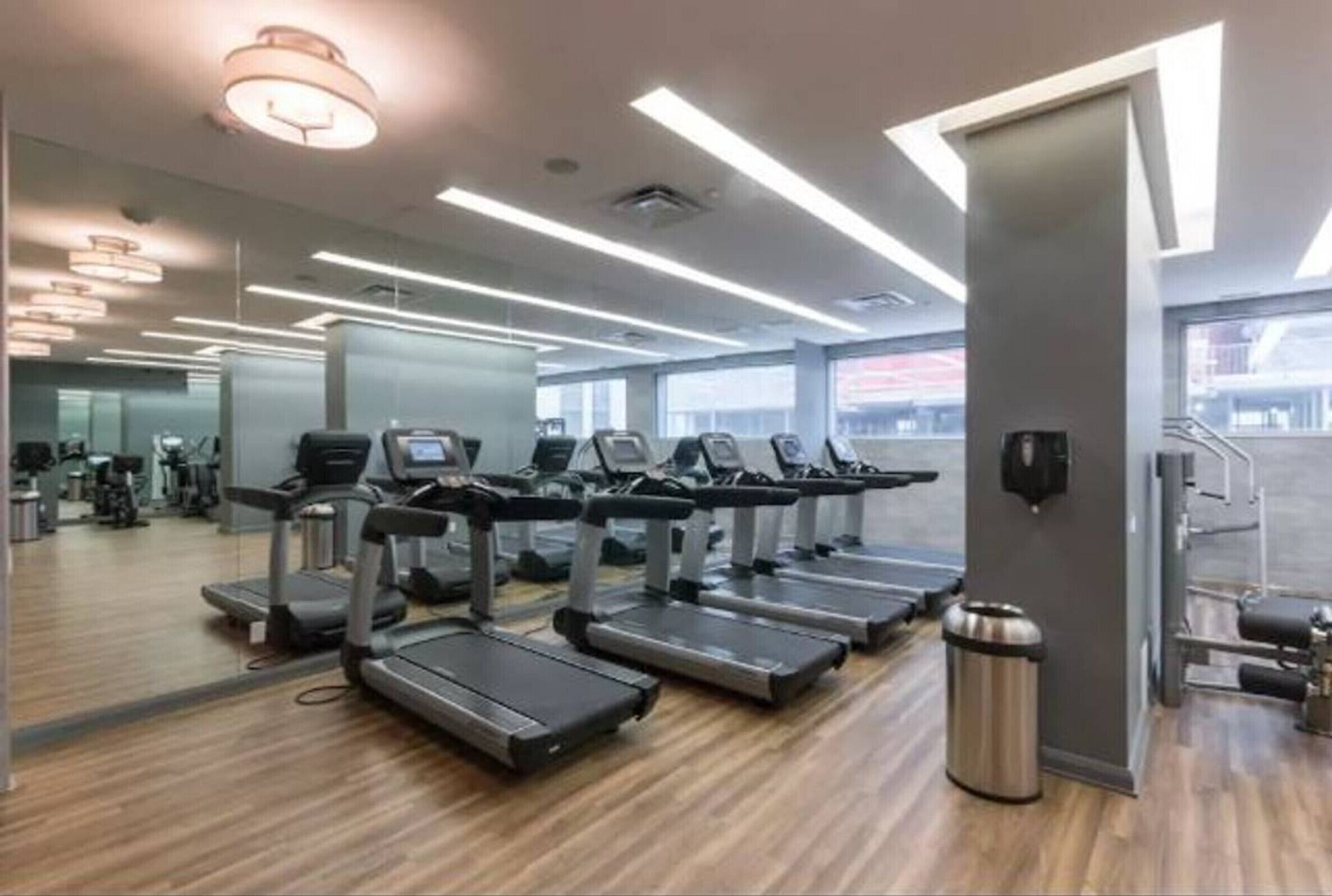 A modern gym with treadmills, exercise equipment, and a large window providing natural light.