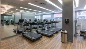Une salle de sport moderne équipée de tapis de course, d’appareils d’exercice et d’une grande fenêtre laissant entrer la lumière naturelle.