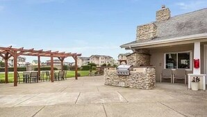 Une terrasse extérieure dotée d’un espace barbecue en pierre, d’une pergola en bois et de coins salon.