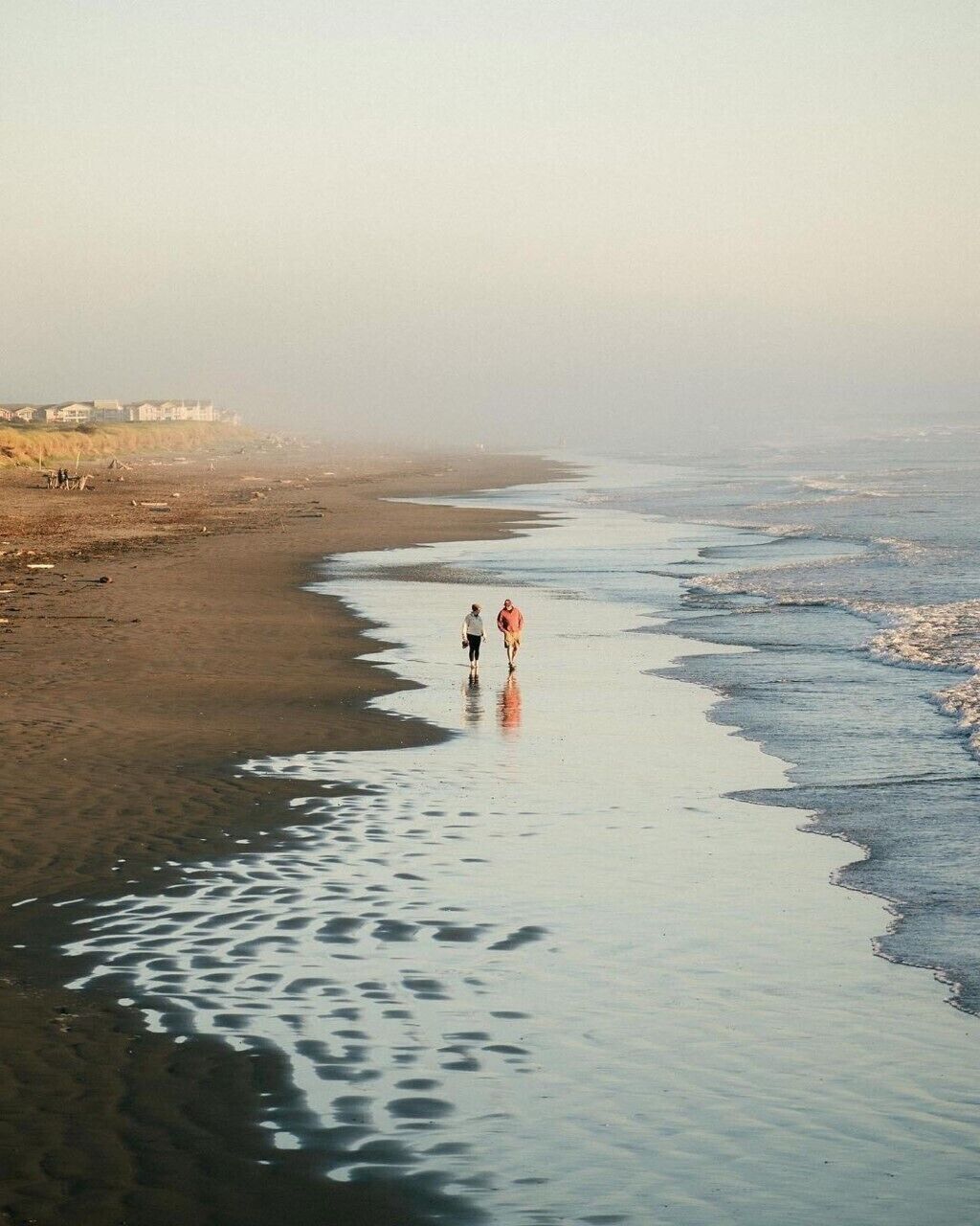 Una playa con dos personas caminando por la orilla.