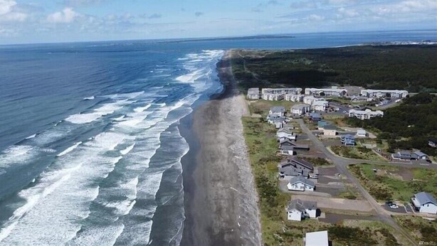 Vue aérienne d’une zone résidentielle côtière, avec des maisons le long du littoral, une plage et l’océan.