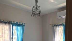 Un dormitori amb un llit, una tauleta de nit, una làmpada i una finestra amb cortines.