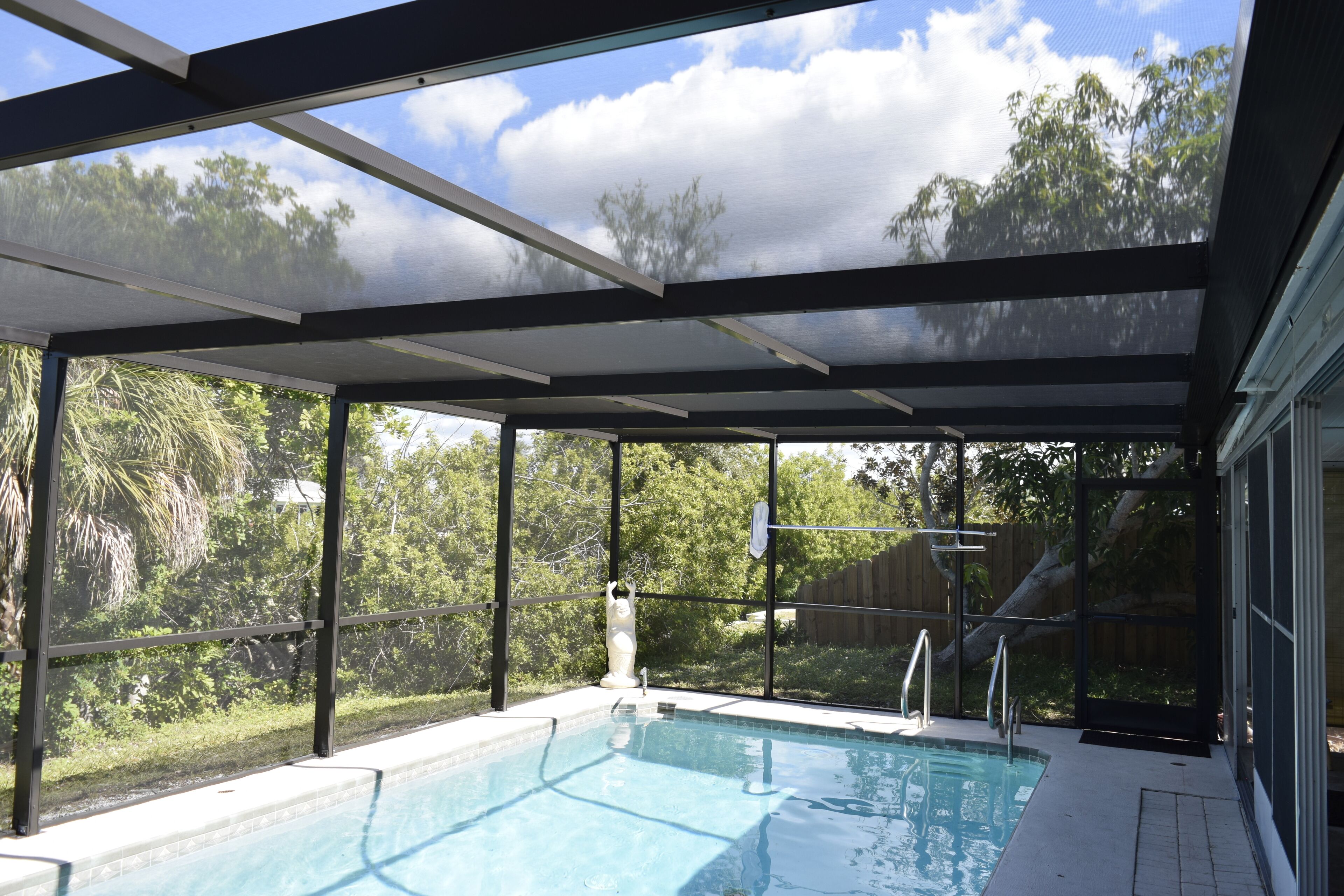 A covered outdoor swimming pool with a view of trees and a clear sky.