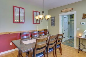 Un espace repas avec une table en bois, des chaises et un banc. Un lustre est suspendu au-dessus de la table, et il y a un panneau sur le mur.