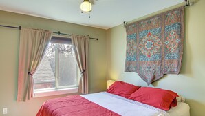 Un dormitorio con cama, cortinas, ventana, tapiz en la pared y ventilador de techo.