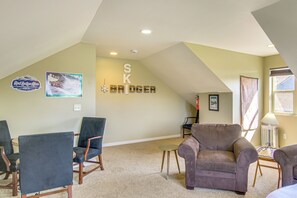 Une pièce avec un plafond en pente, une cheminée, une enseigne fixée au mur portant l’inscription « SK BRIDGE », et un coin repas avec des chaises et une table.