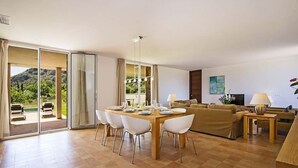A spacious living area with a dining table set for four, a sofa, and a TV. - Luxury modern stone clad Villa with swimming pool and mountain views (POLLENSA)