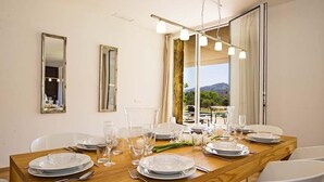 A dining area with a wooden table set for four, two wall mirrors, and a view of the outdoors. - Luxury modern stone clad Villa with swimming pool and mountain views (POLLENSA)