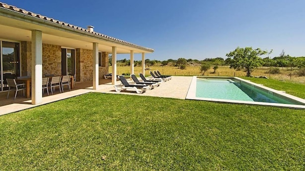 A modern house with a covered patio, a swimming pool, and a well-maintained lawn. - Luxury modern stone clad Villa with swimming pool and mountain views (POLLENSA)
